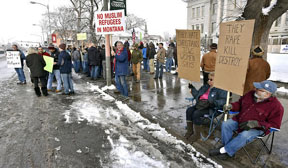 Dee and John Gibney, right, sit holding anti-refugee signs and watch a small group of counter protesters at far left during a rally in Missoula